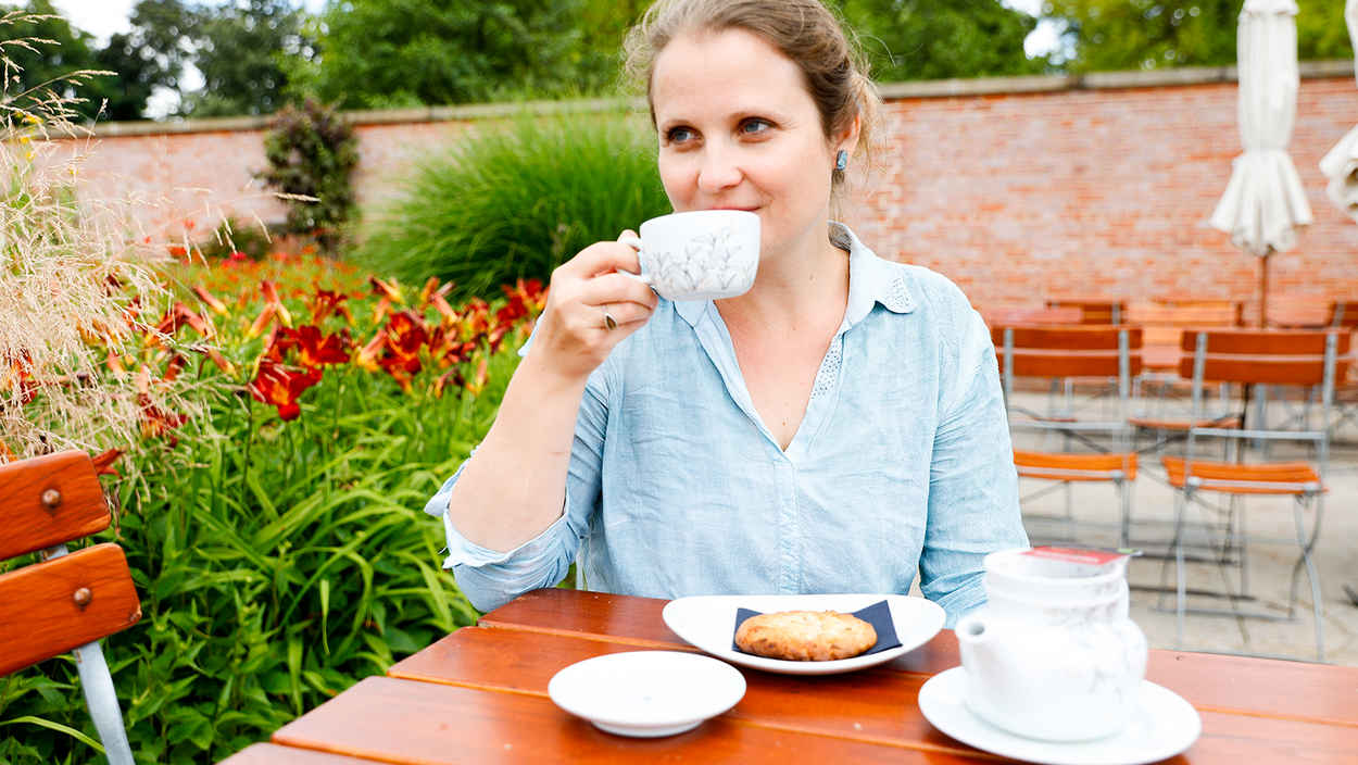 Eine Frau trinkt draußen im Cottage Tee, vor ihr liegt ein Cookie