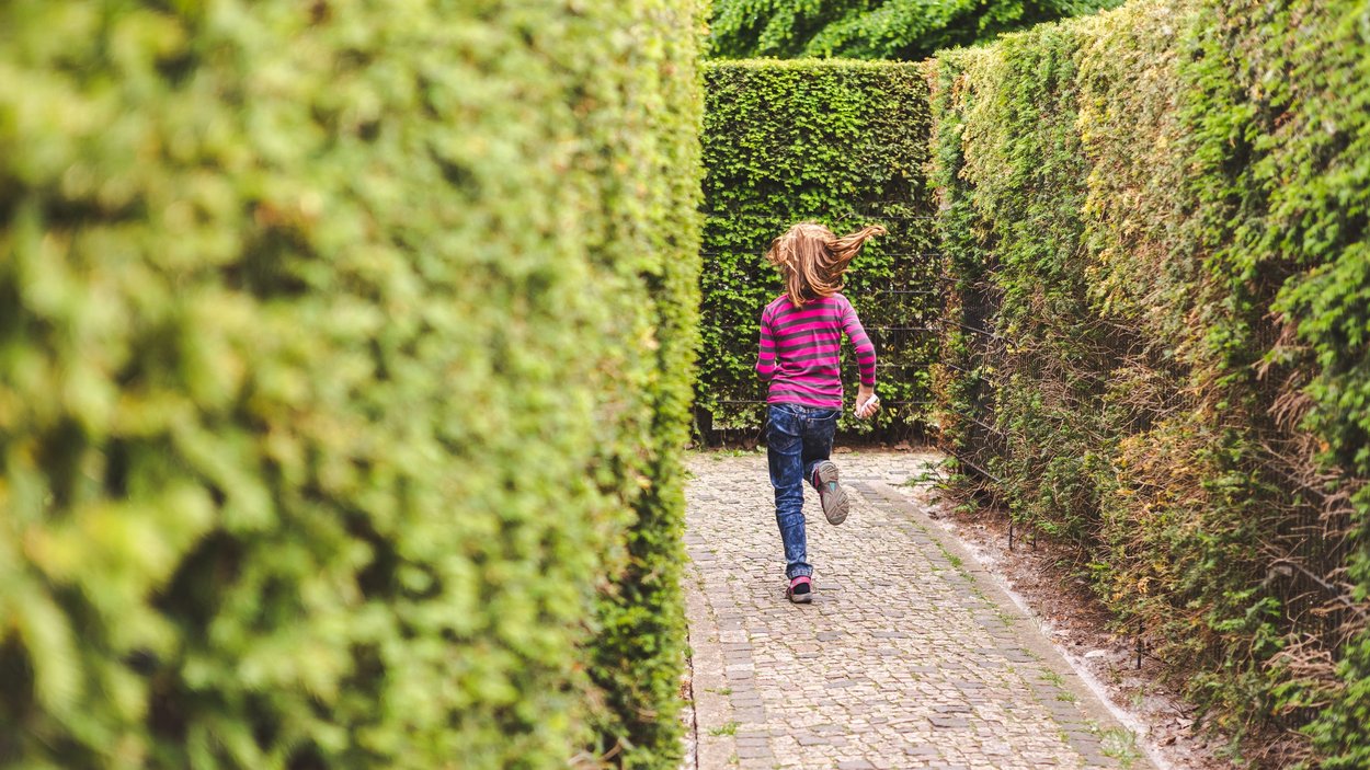 Kind läuft durch Irrgarten aus grünen Hecken in den Gärten der Welt